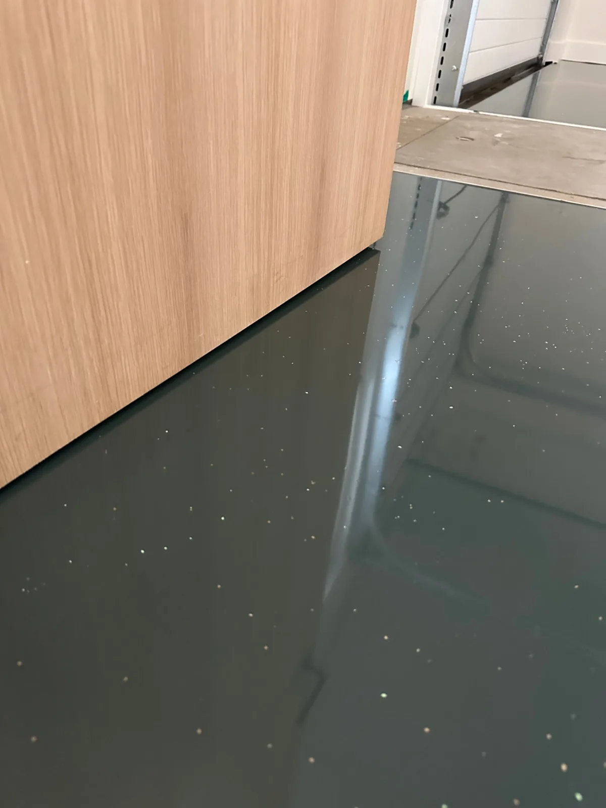 Hoogglanzende epoxyvloer met kleurvlokken langs een houten kastwand