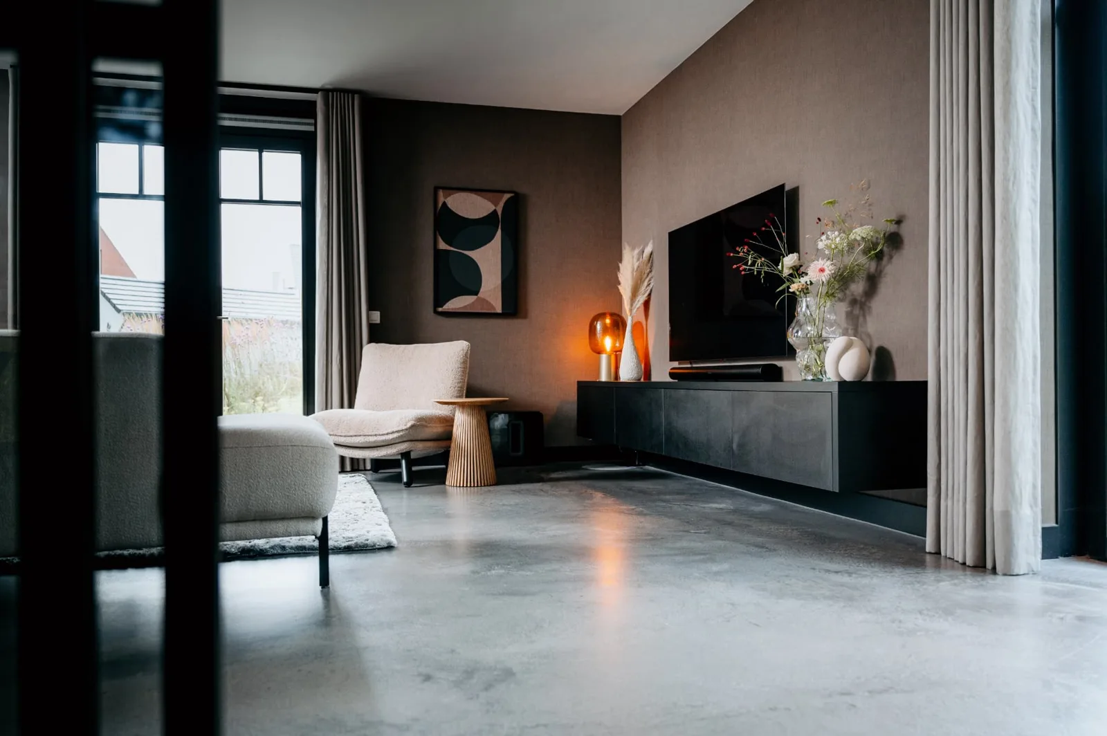 Woonkamer met levendige M2 Architop gietvloer, beige fauteuil en zwart tv-meubel