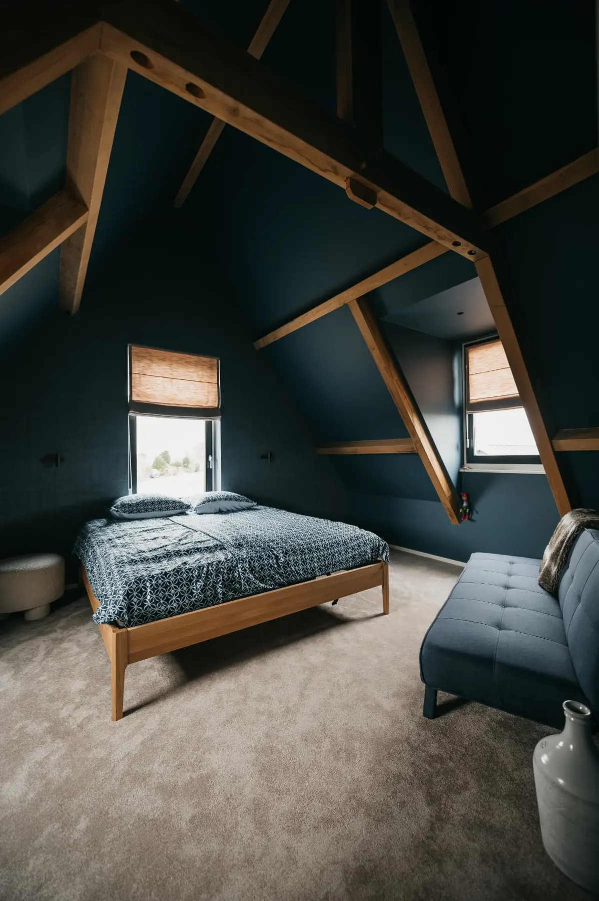 Slaapkamer met donkerblauwe wanden, houten spanten en een zachte tapijtvloer