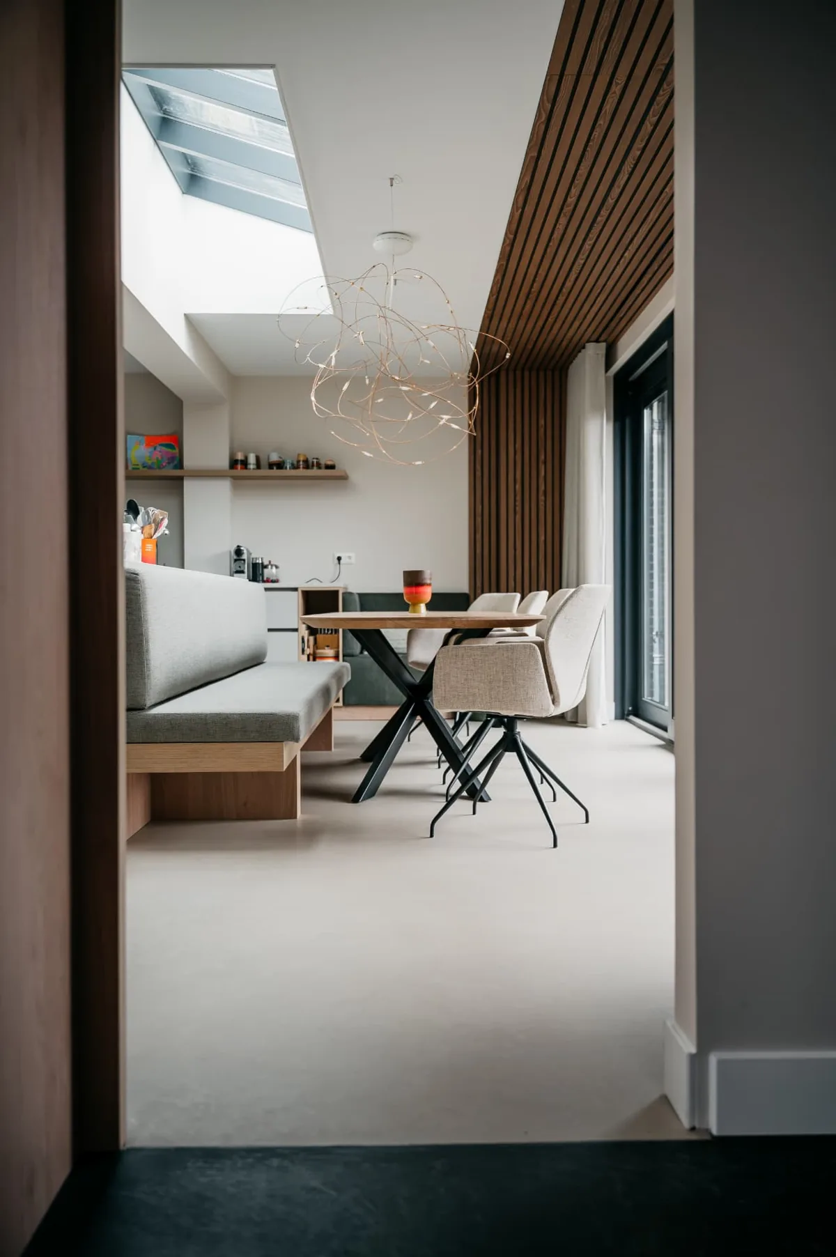 Doorkijk naar eethoek met lichte Micro-Quartz gietvloer en houten lamellenwand
