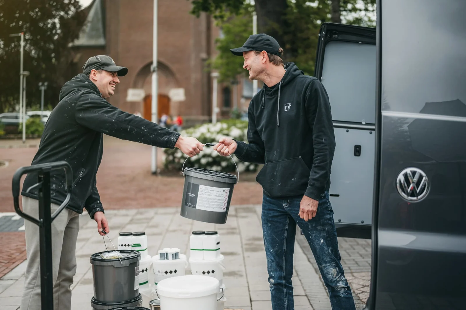 Twee monteurs laden emmers gietvloermateriaal uit de bus