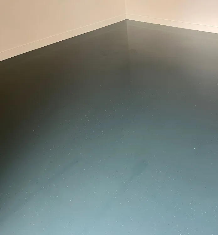 Egale grijze epoxygietvloer met witte plinten in een lege ruimte
