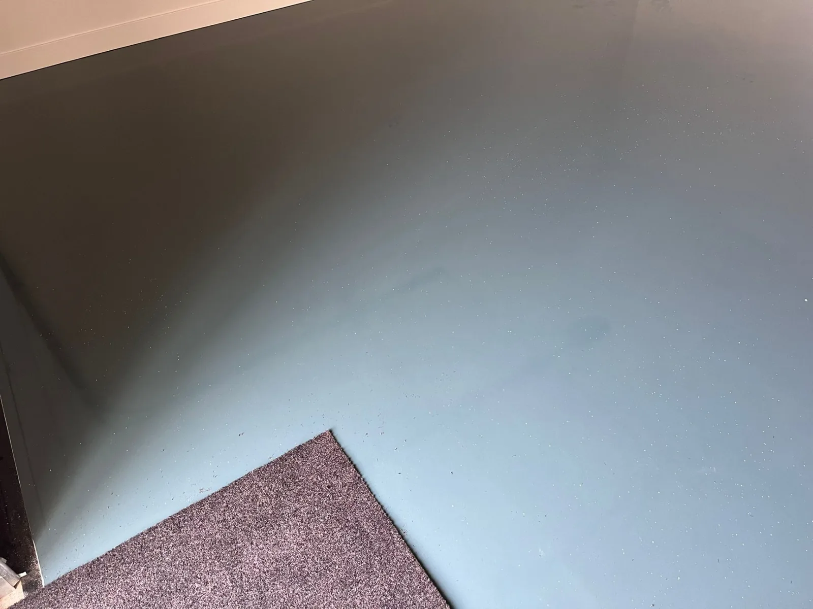 Gladde grijze epoxygietvloer met een schoonloopmat in de hoek