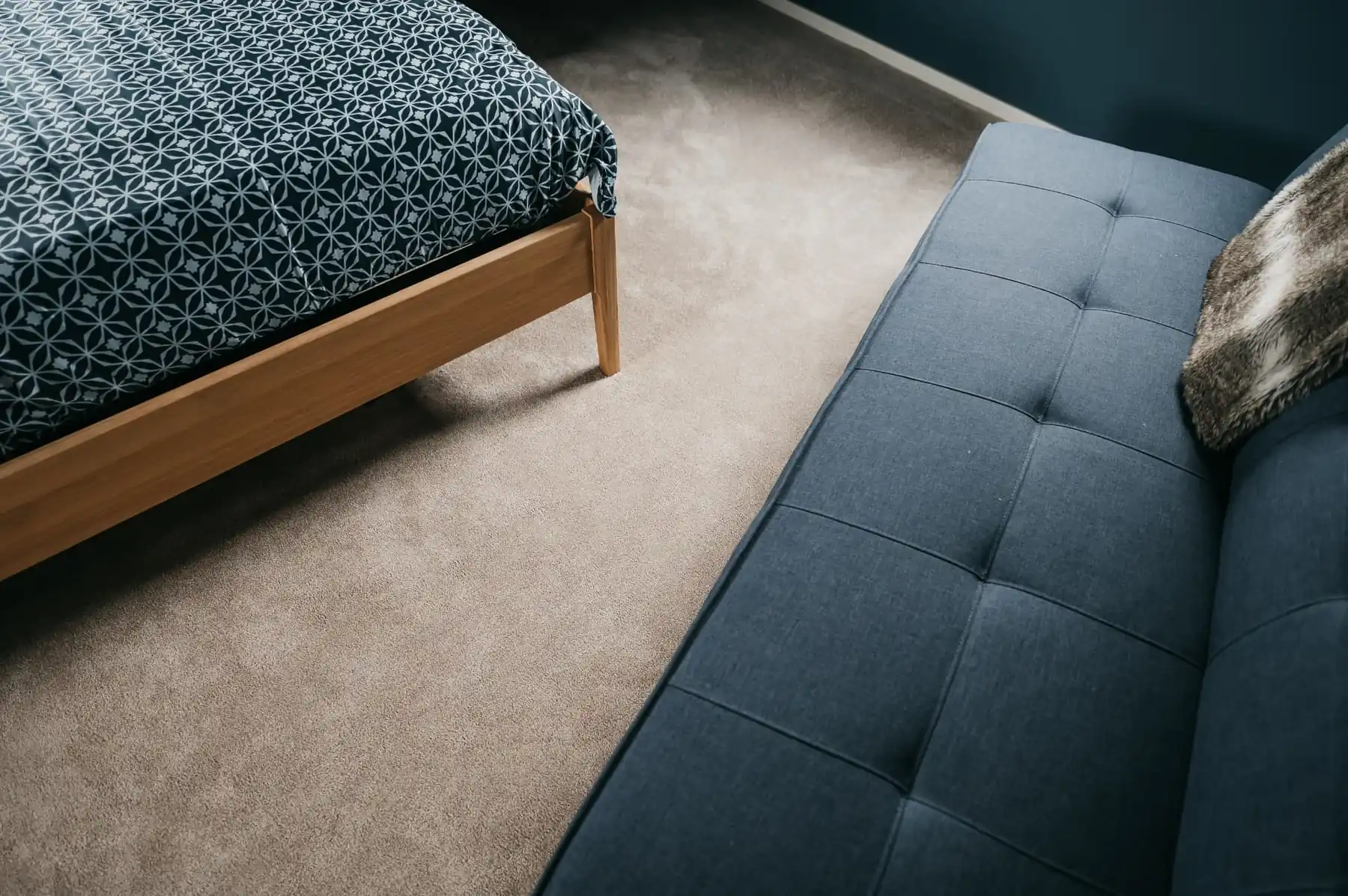 Beige tapijtvloer in een slaapkamer bij een houten bed en blauwe bank